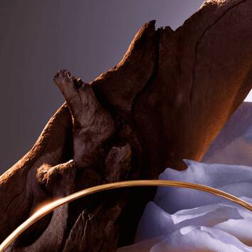 Un pezzo di legno scolpito con un cerchio dorato e morbide pieghe di tessuto blu sullo sfondo.