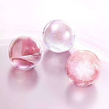 Tre sfere di gel trasparente e colorato in tonalita rosa e viola, decorate con bolle d'aria su uno sfondo morbido.