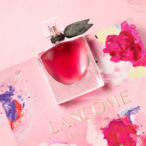 Bottiglia di profumo Lancome su sfondo rosa con dettagli artistici, rappresenta eleganza e stile.