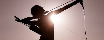 Silhouette di un arciere che tende una corda d'arco, con il sole che splende dietro di lui.