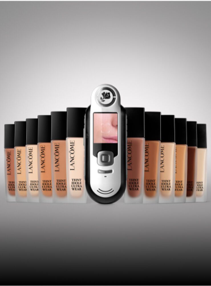 Immagine di vari fondotinta Lancome disposti in fila, con un dispositivo che mostra una pelle vicino al centro.