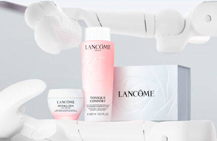 A pink-hued background featuring two Lancome Hydra Zen skincare products: a moisturizer in a jar and a spray mist in a bottle.
