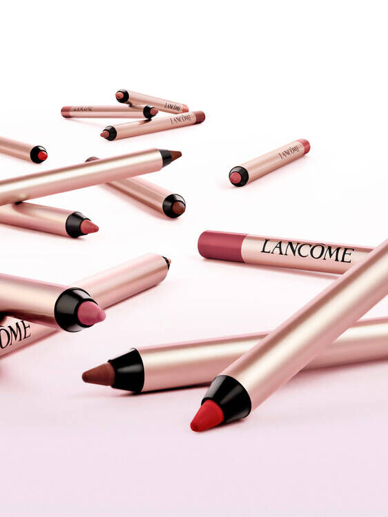 Un gruppo di matite per labbra Lancome di vari colori, disposte su uno sfondo rosa chiaro.