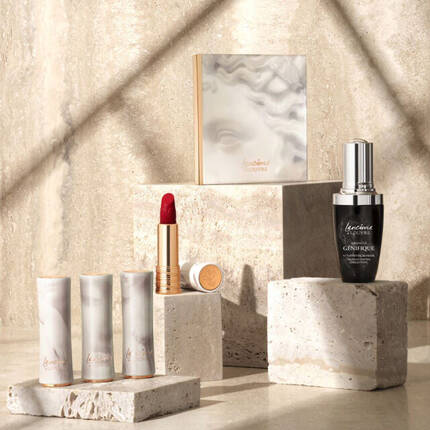 Immagine di prodotti cosmetici elegantemente disposti su blocchi di pietra, con un rossetto rosso, una palette e un siero viso, su uno sfondo di marmo chiaro.
