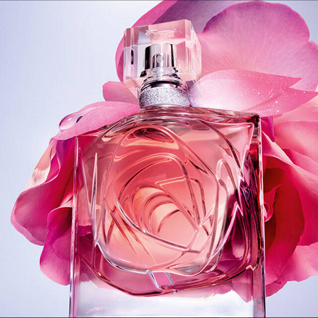 Una bottiglia di profumo elegante circondata da una grande rosa rosa su uno sfondo sfumato.