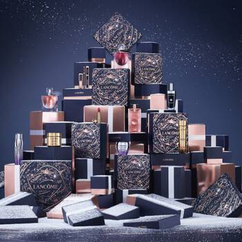 Una piramide di eleganti confezioni regalo Lancome su sfondo blu scuro, con decorazioni e un'atmosfera festiva.