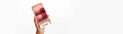 Una mano che tiene uno smartphone con un'immagine di labbra truccate in diverse tonalita di rossetto del marchio Lancome.