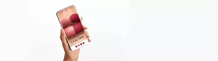 Una mano che tiene uno smartphone con un'immagine di labbra truccate in diverse tonalita di rossetto del marchio Lancome.