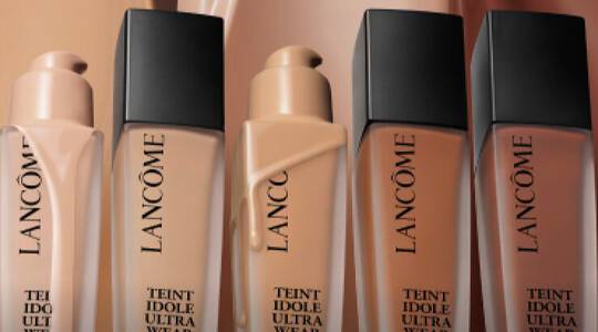 Immagine di tre flaconi di fondotinta Lancome Teint Idole Ultra Wear su uno sfondo di tonalita nude.