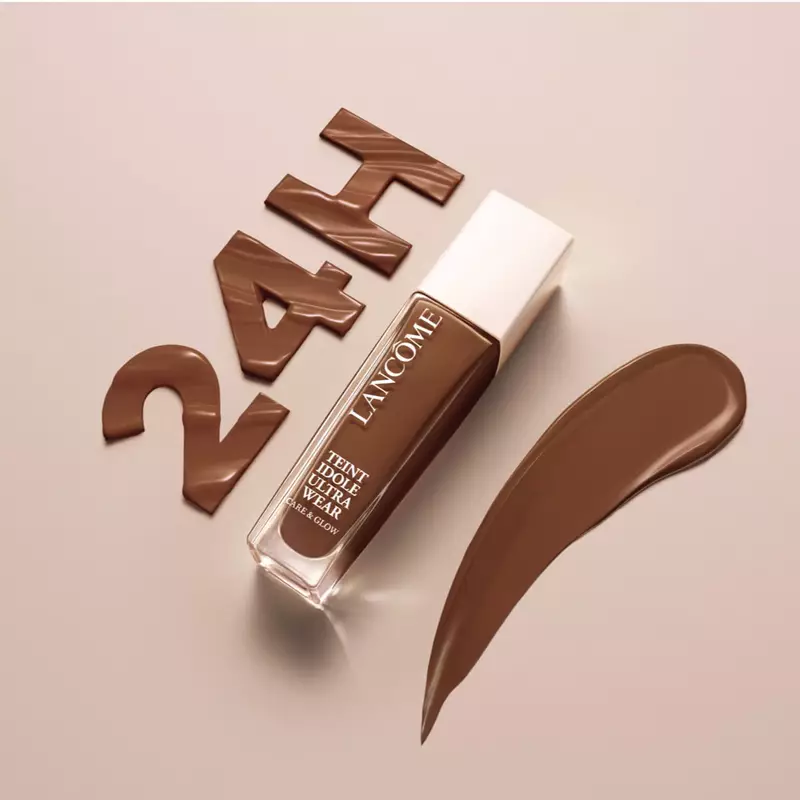 Immagine di un fondotinta Lancome con la scritta "24H" in marrone, accanto a una striscia di prodotto su uno sfondo beige.