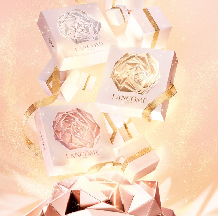 Immagine di eleganti scatole regalo di Lancome con design a forma di rosa, circondate da piccoli pacchetti e un fondo luminato.