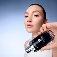 Donna con pelle radiosa che tiene un flacone di Lancome Genifique Ultimate.